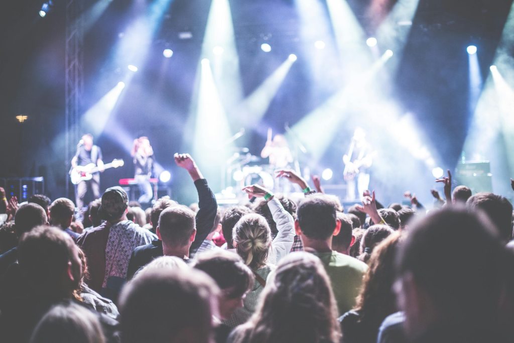Dynamische Konzertszene mit einem begeisterten Publikum und einer Band, die unter hellem Scheinwerferlicht spielt.