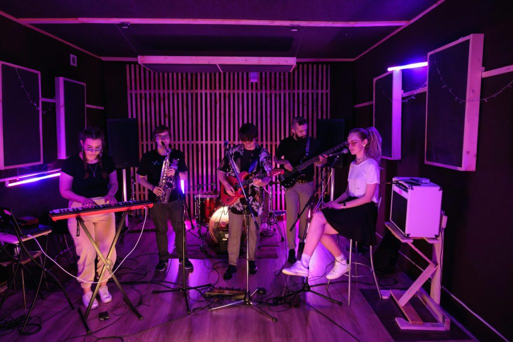 Eine dynamische junge Band probt mit Musikinstrumenten unter Neonlicht in einem Studio.